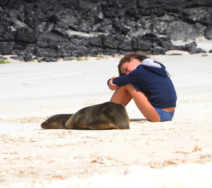Young girl sitting next to a sleepy Galapagos sea lion pup