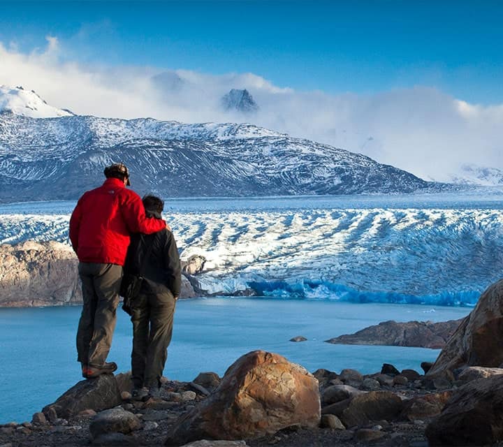 Couple standing on cliffside to view glacier field