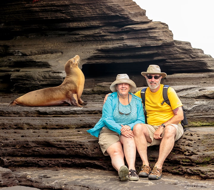 A couple sitting next to a Galapagos Sea Lion on a cruise adventure