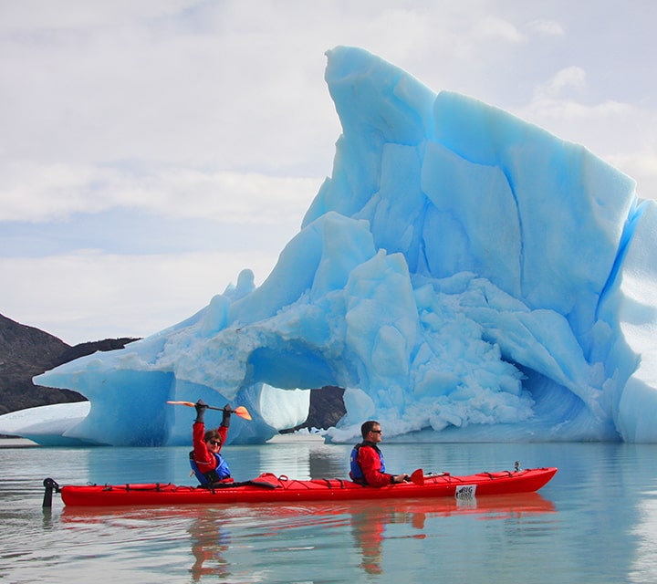 Tall glacier set behind two men in a red kayak in Patagonia