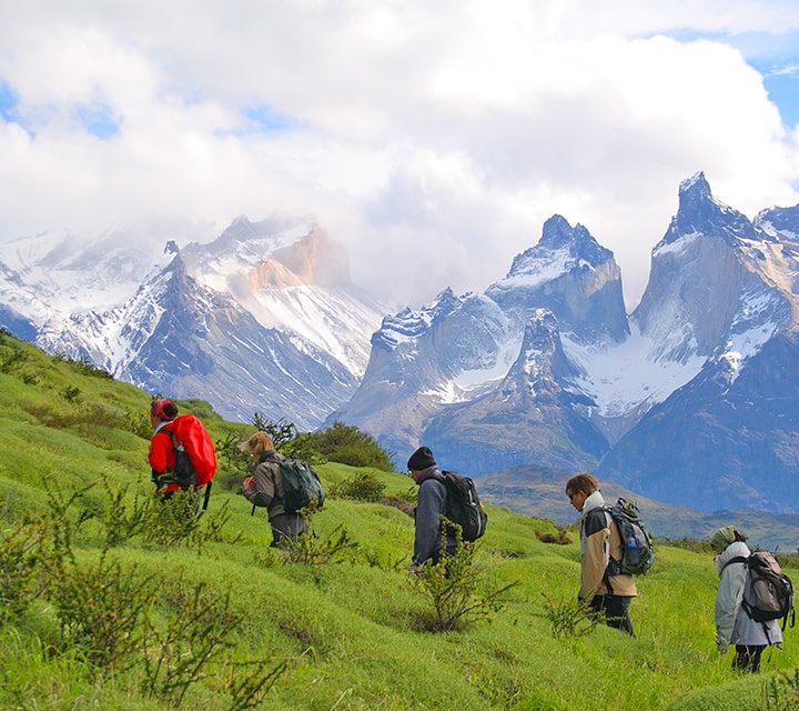 A small group of travelers going uphill in the rolling Patagonian pampas with a dramatic backdrop of Torres del Paine National Park