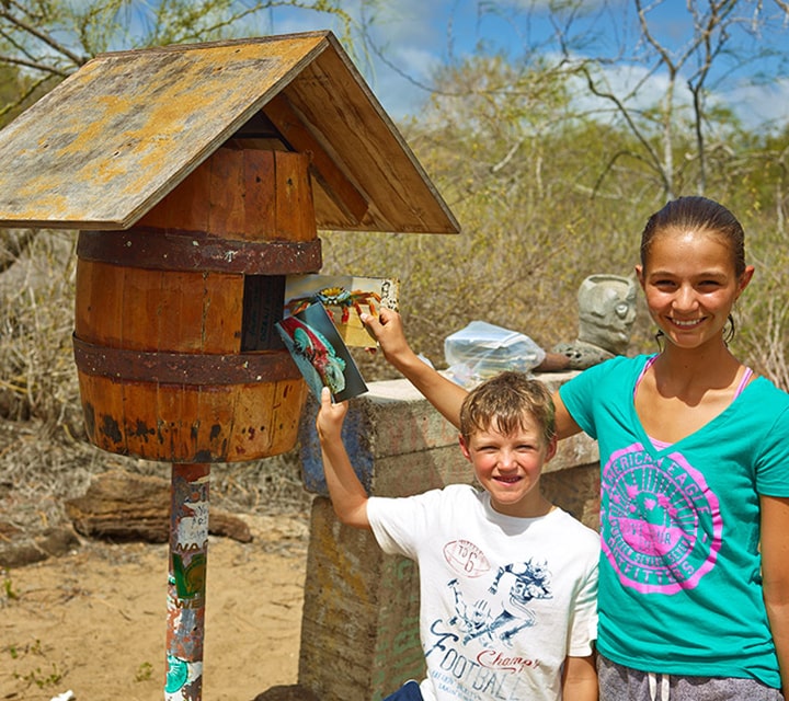 Kids dropping off unstamped letters at Post Office Bay in Floreana Island, Galapagos 