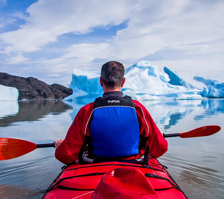 Man in red kayak paddling next to glaciers in Patagonia