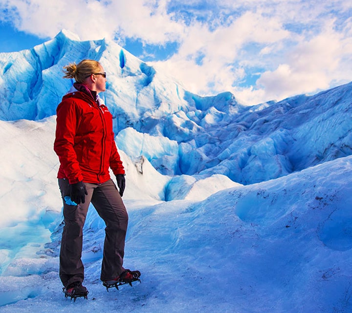 A women wearing a red jacket with traction cleats while enjoying the peace and quiet on a Glacier in Patagonia