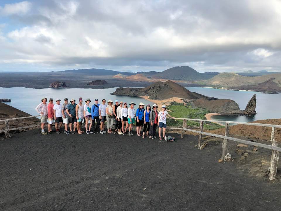 A group of family & friends overlooking view of Pinnacle Rock, but also Daphne Major, Daphne Mindor and the rest of Santiago Island from the summit of Bartolome Island