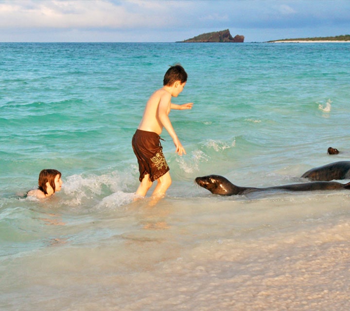 Two kids playing in the water alongside a sea lion in the Galapagos 