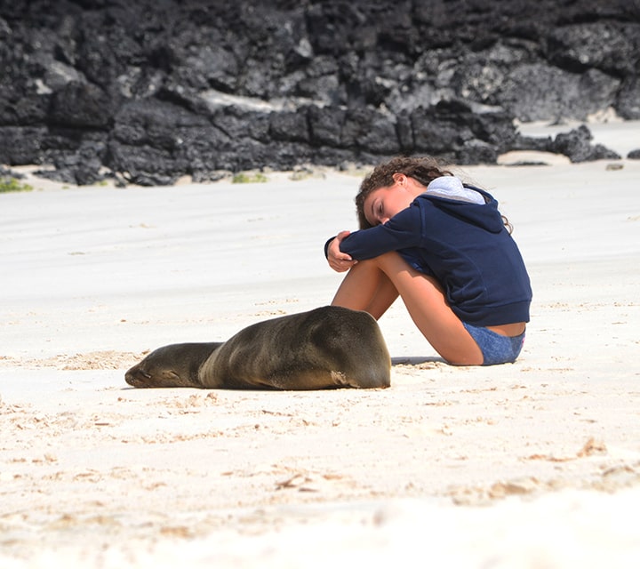 Young girl taking a nap next to a Sea Lion on a white sand beach in the Galapagos