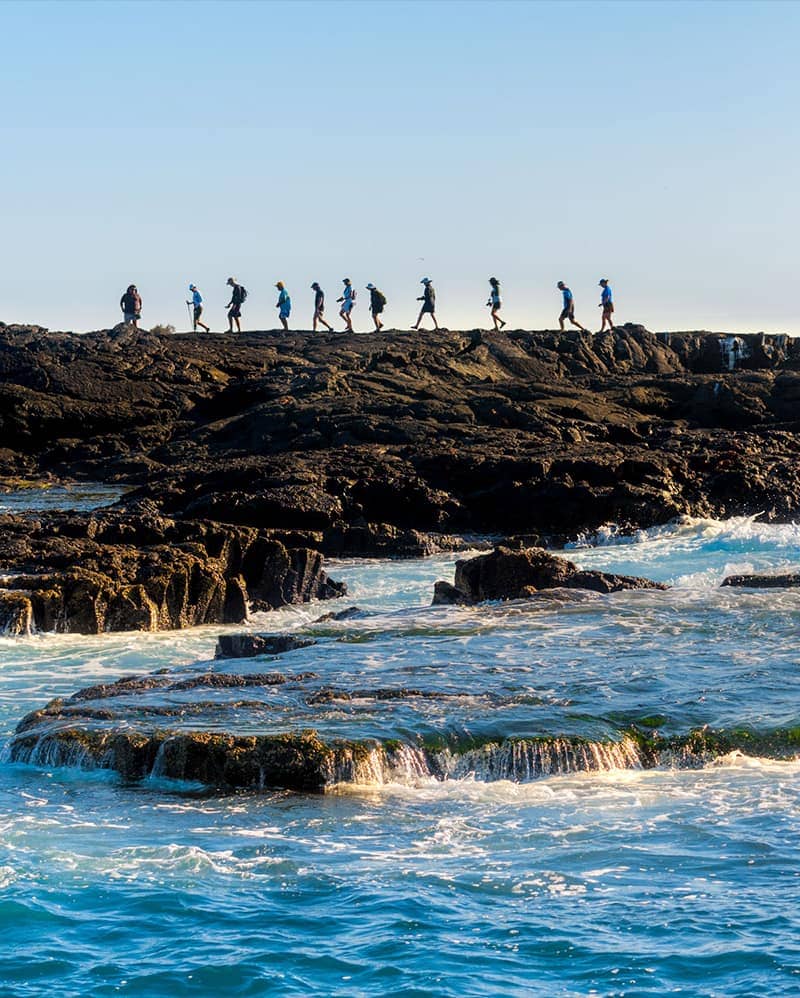 Small group of people walking with a guide on the rocky shores of Galapagos with beachy surroundings