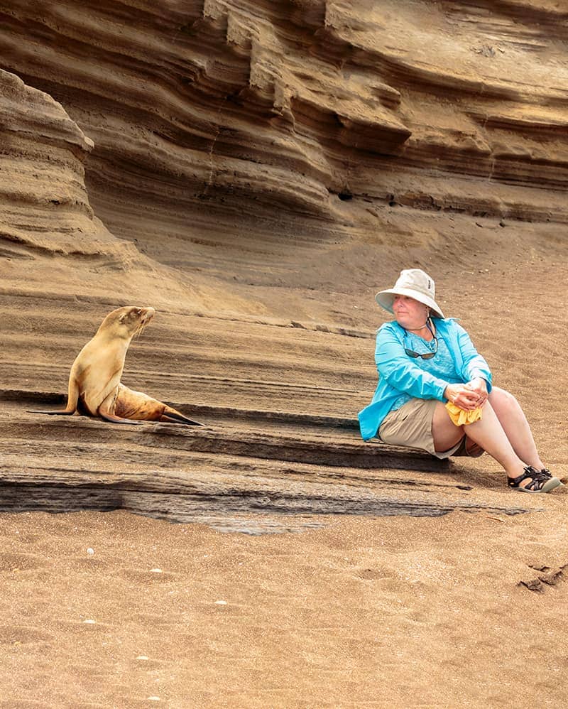 Woman sitting next to a sea lion with scenic Galapagos backdrop